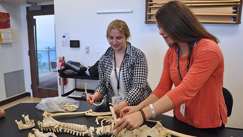 Two female high school students examine a skeleton on a table