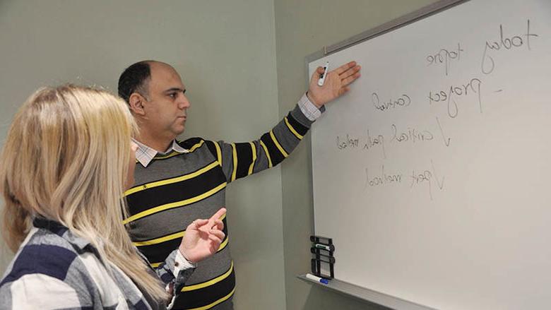 An instructor and student work together in the classroom at a whiteboard