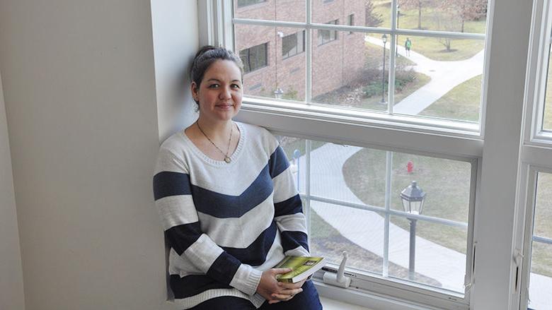 Female student sits in third story window overlooking quad